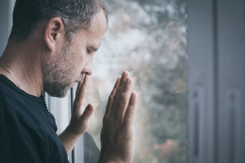 Man der aus dem Fenster schaut und traurig ist.