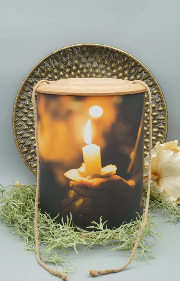 Fotourne mit Holzboden und Holzdeckel mit einer Hand die eine brennende Kerze hält bedruckt mit Ablassschnur